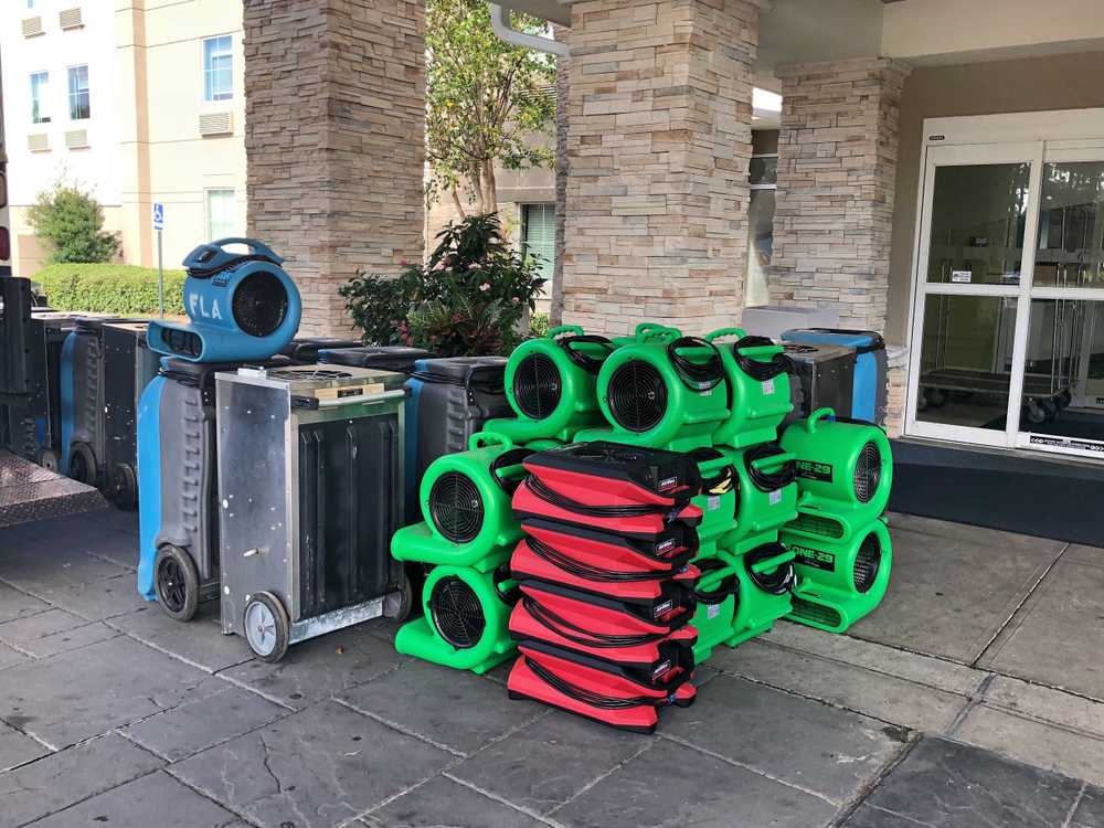 Stacked industrial fans and dehumidifiers outside building entrance.